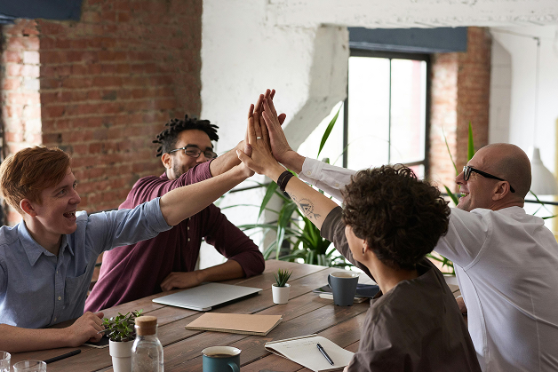 Four diverse team members enthusiastically high-five across a table, showing unity and celebration